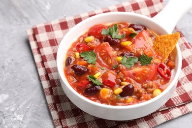 Photo of Tasty chili con carne in bowl and nachos on grey textured table, closeup