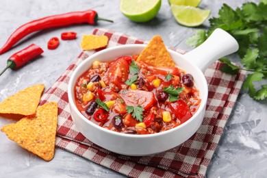 Photo of Tasty chili con carne in bowl and nachos on grey textured table, closeup