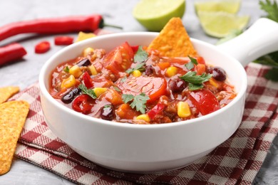 Photo of Tasty chili con carne in bowl and nachos on grey textured table, closeup