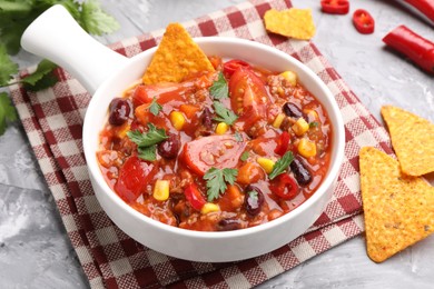 Photo of Tasty chili con carne in bowl and nachos on grey textured table, closeup