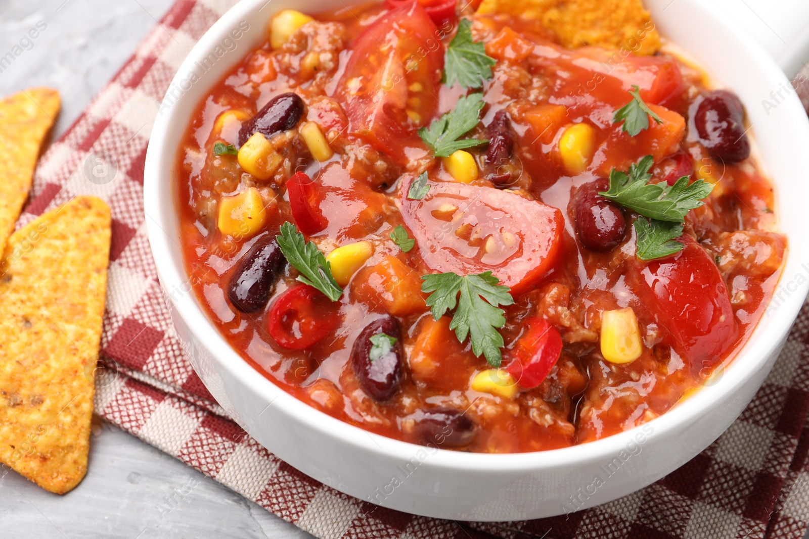 Tasty chili con carne in bowl and nachos on grey textured table, closeup Photo of Tasty chili con carne in bowl and nachos on grey textured table, closeup