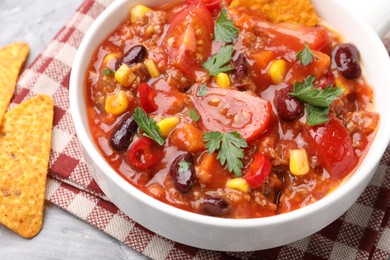 Photo of Tasty chili con carne in bowl and nachos on grey textured table, closeup
