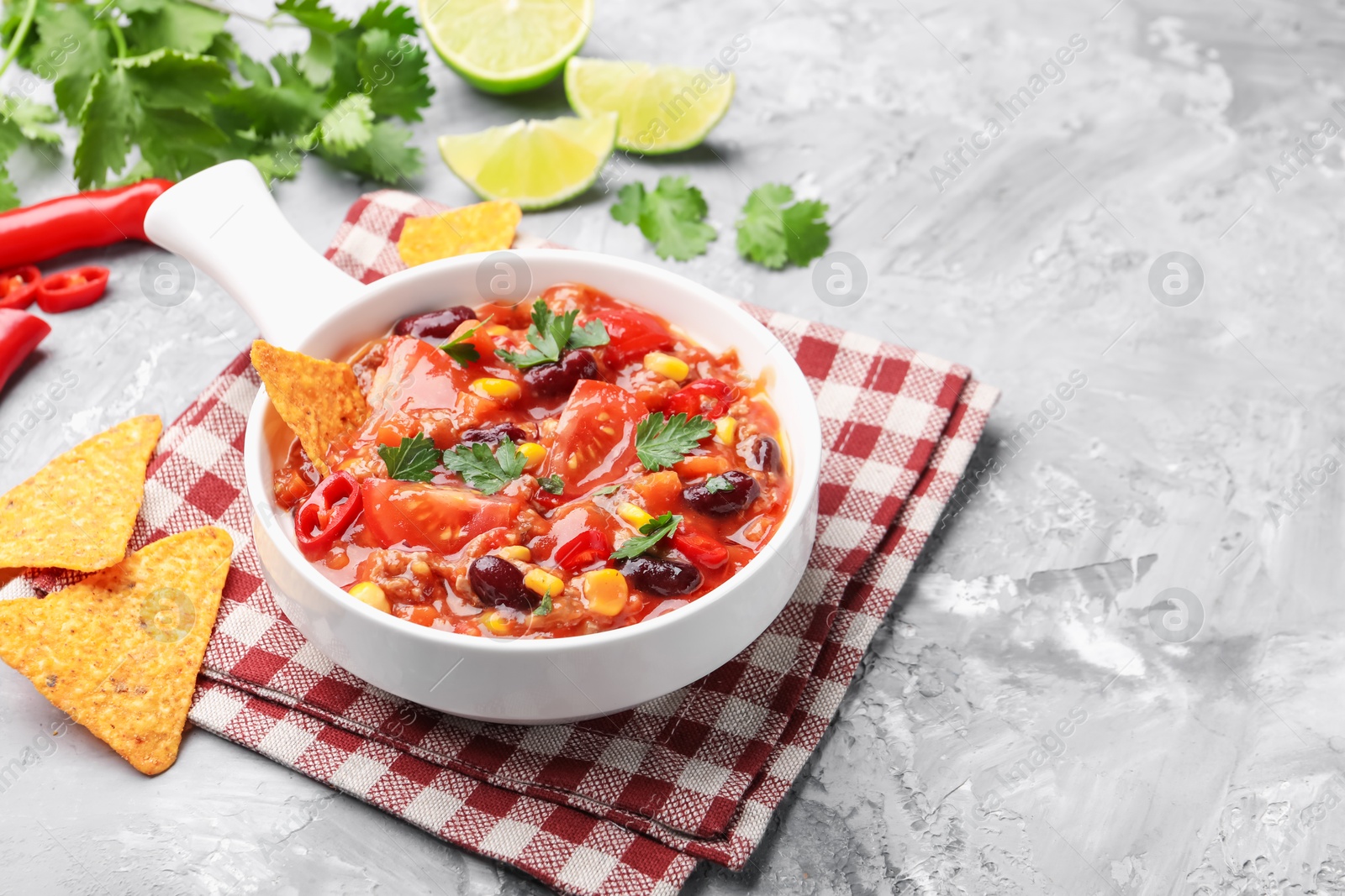 Tasty chili con carne in bowl and nachos on grey textured table, closeup. Space for text Photo of Tasty chili con carne in bowl and nachos on grey textured table, closeup. Space for text