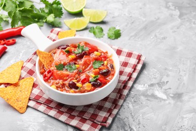 Photo of Tasty chili con carne in bowl and nachos on grey textured table, closeup. Space for text