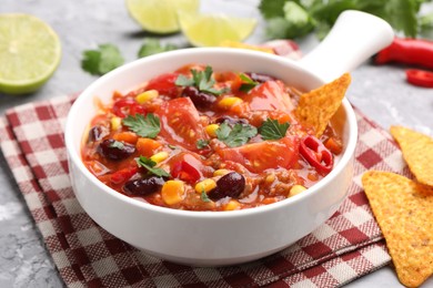Photo of Tasty chili con carne in bowl and nachos on grey textured table, closeup
