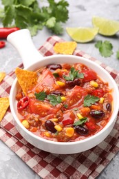 Photo of Tasty chili con carne in bowl and nachos on grey textured table, closeup