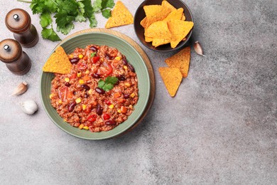 Photo of Tasty chili con carne in bowl and nachos on grey table, flat lay. Space for text