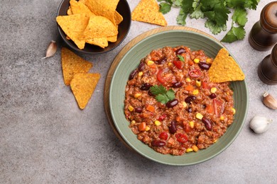 Photo of Tasty chili con carne in bowl and nachos on grey table, flat lay. Space for text