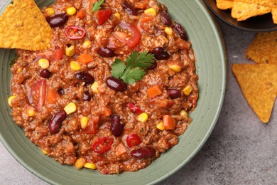 Photo of Tasty chili con carne in bowl and nachos on grey table, flat lay