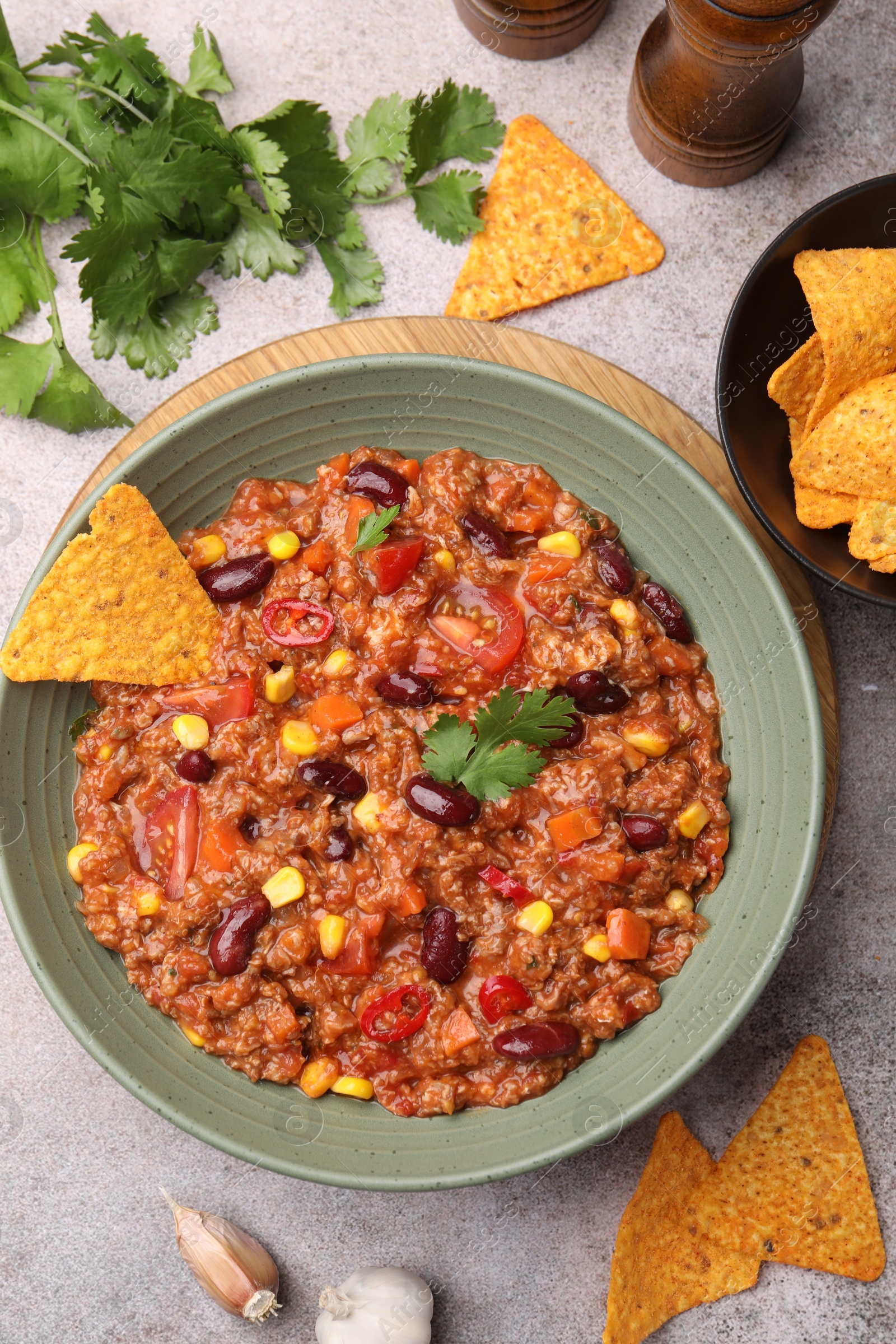 Tasty chili con carne in bowl and nachos on grey table, flat lay Photo of Tasty chili con carne in bowl and nachos on grey table, flat lay