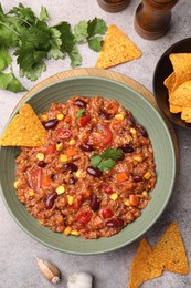Photo of Tasty chili con carne in bowl and nachos on grey table, flat lay