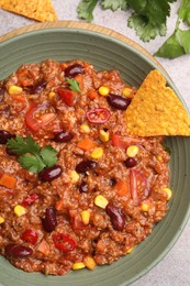 Photo of Tasty chili con carne in bowl and nachos on grey table, flat lay