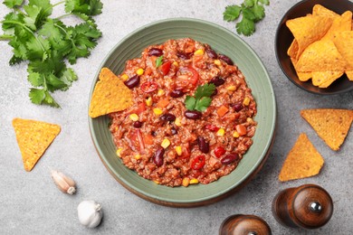 Photo of Tasty chili con carne in bowl and nachos on grey table, flat lay