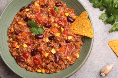 Photo of Tasty chili con carne in bowl and nachos on grey table, flat lay