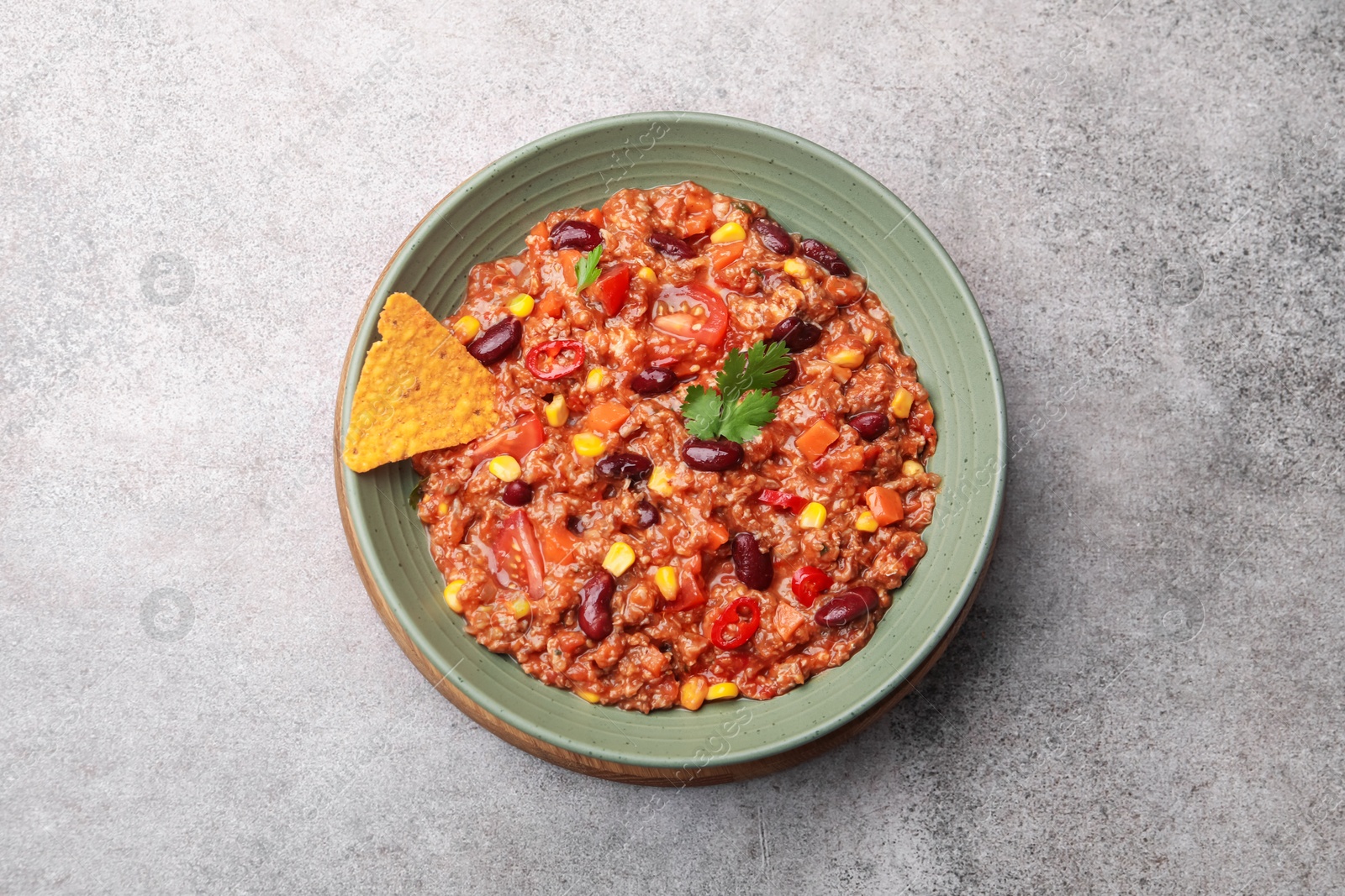 Tasty chili con carne in bowl and nachos on grey table, top view Photo of Tasty chili con carne in bowl and nachos on grey table, top view