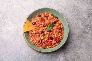 Photo of Tasty chili con carne in bowl and nachos on grey table, top view