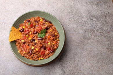 Photo of Tasty chili con carne in bowl and nachos on grey table, top view. Space for text