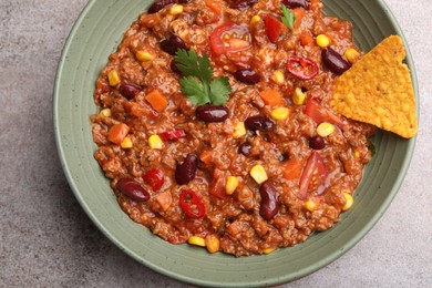 Photo of Tasty chili con carne in bowl and nachos on grey table, top view