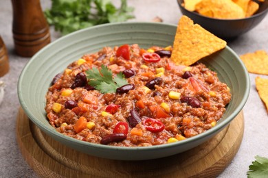 Photo of Tasty chili con carne in bowl and nachos on grey table, closeup