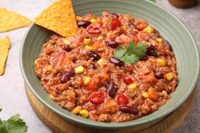 Photo of Tasty chili con carne in bowl and nachos on grey table, closeup