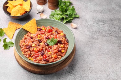Photo of Tasty chili con carne in bowl and nachos on grey table, closeup. Space for text