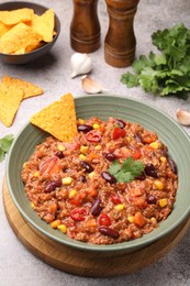 Photo of Tasty chili con carne in bowl and nachos on grey table, closeup