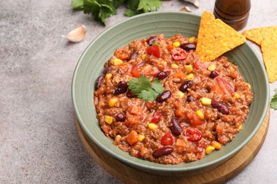 Photo of Tasty chili con carne in bowl and nachos on grey table, closeup. Space for text