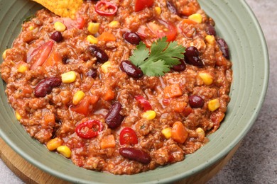 Photo of Tasty chili con carne in bowl and nachos on grey table, closeup
