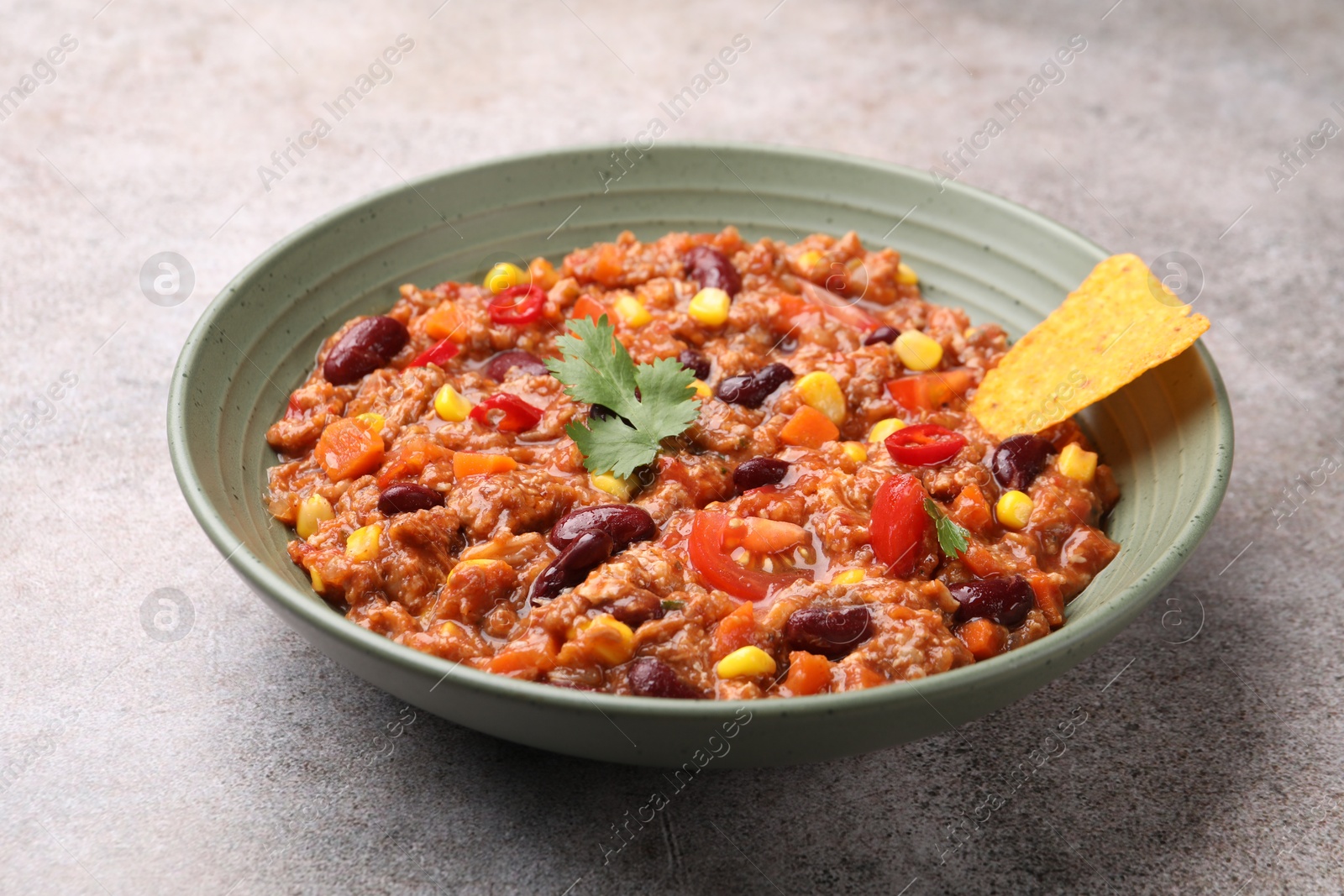 Tasty chili con carne in bowl and nachos on grey table, closeup Photo of Tasty chili con carne in bowl and nachos on grey table, closeup