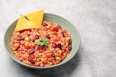Photo of Tasty chili con carne in bowl and nachos on grey table, closeup. Space for text