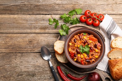 Photo of Tasty chili con carne in bowl, ingredients and bread on wooden table, flat lay. Space for text
