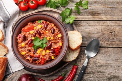 Photo of Tasty chili con carne in bowl, ingredients and bread on wooden table, flat lay. Space for text