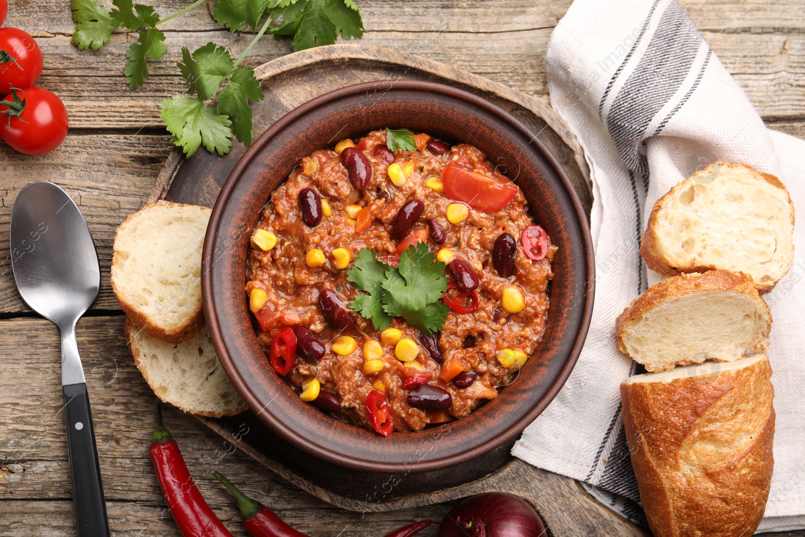 Tasty chili con carne in bowl, ingredients and bread on wooden table, flat lay Photo of Tasty chili con carne in bowl, ingredients and bread on wooden table, flat lay