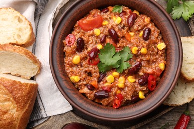 Photo of Tasty chili con carne in bowl, ingredients and bread on wooden table, flat lay