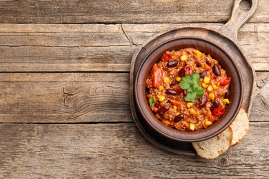Photo of Tasty chili con carne in bowl and bread slices on wooden table, top view. Space for text
