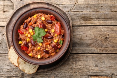 Photo of Tasty chili con carne in bowl and bread slices on wooden table, top view. Space for text