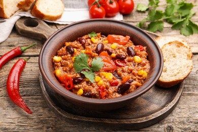 Photo of Tasty chili con carne in bowl, ingredients and bread on wooden table, closeup