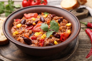 Photo of Tasty chili con carne in bowl on wooden table, closeup