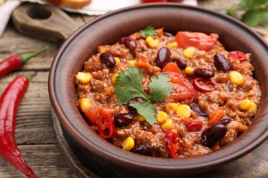 Photo of Tasty chili con carne in bowl on wooden table, closeup