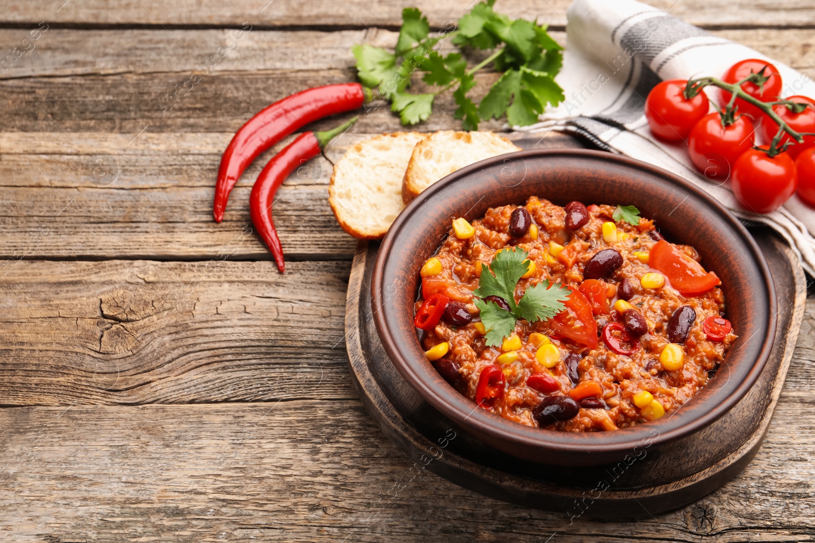 Tasty chili con carne in bowl and ingredients on wooden table, closeup. Space for text Photo of Tasty chili con carne in bowl and ingredients on wooden table, closeup. Space for text
