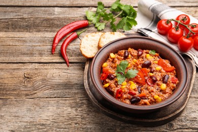 Photo of Tasty chili con carne in bowl and ingredients on wooden table, closeup. Space for text