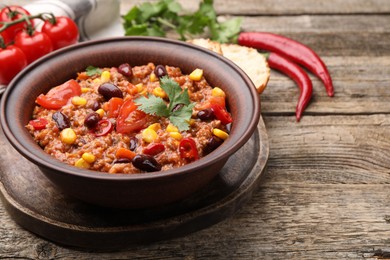 Photo of Tasty chili con carne in bowl and ingredients on wooden table, closeup. Space for text
