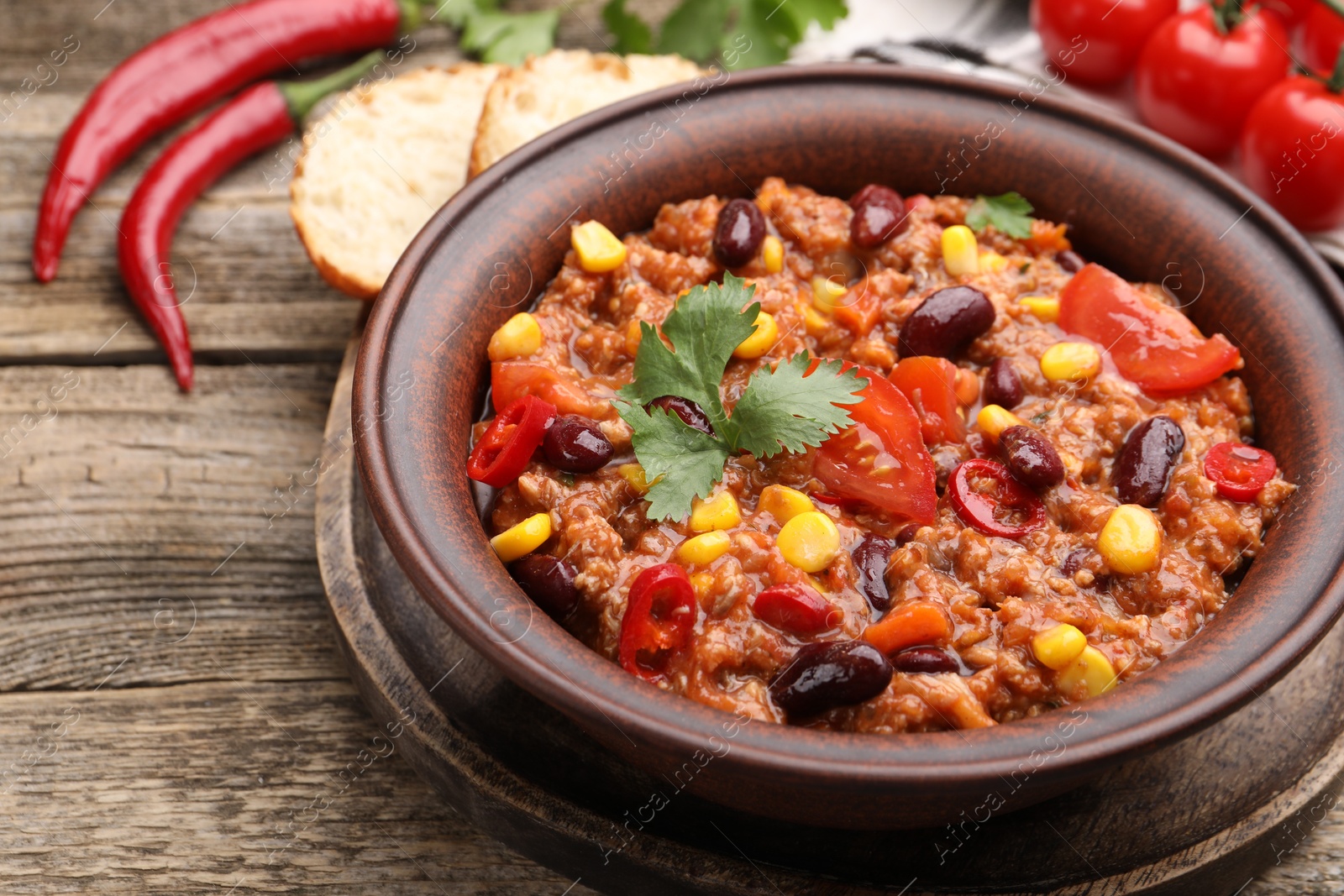 Tasty chili con carne in bowl, ingredients and bread on wooden table, closeup Photo of Tasty chili con carne in bowl, ingredients and bread on wooden table, closeup