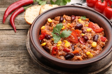 Photo of Tasty chili con carne in bowl, ingredients and bread on wooden table, closeup