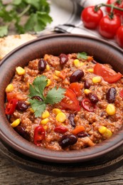 Photo of Tasty chili con carne in bowl on wooden table, closeup