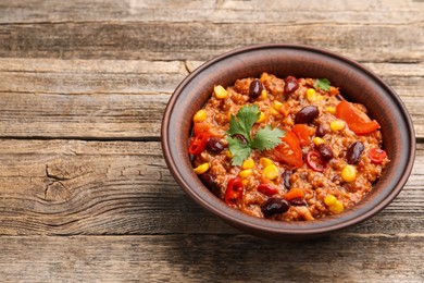 Photo of Tasty chili con carne in bowl on wooden table, closeup. Space for text