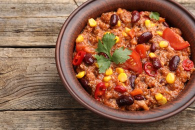 Photo of Tasty chili con carne in bowl on wooden table, closeup. Space for text