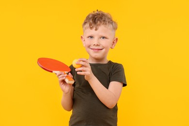 Photo of Little boy with ping pong racket and ball on yellow background