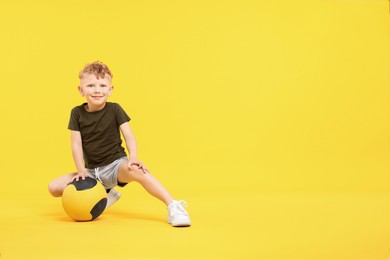 Photo of Little boy with medicine ball on yellow background, space for text