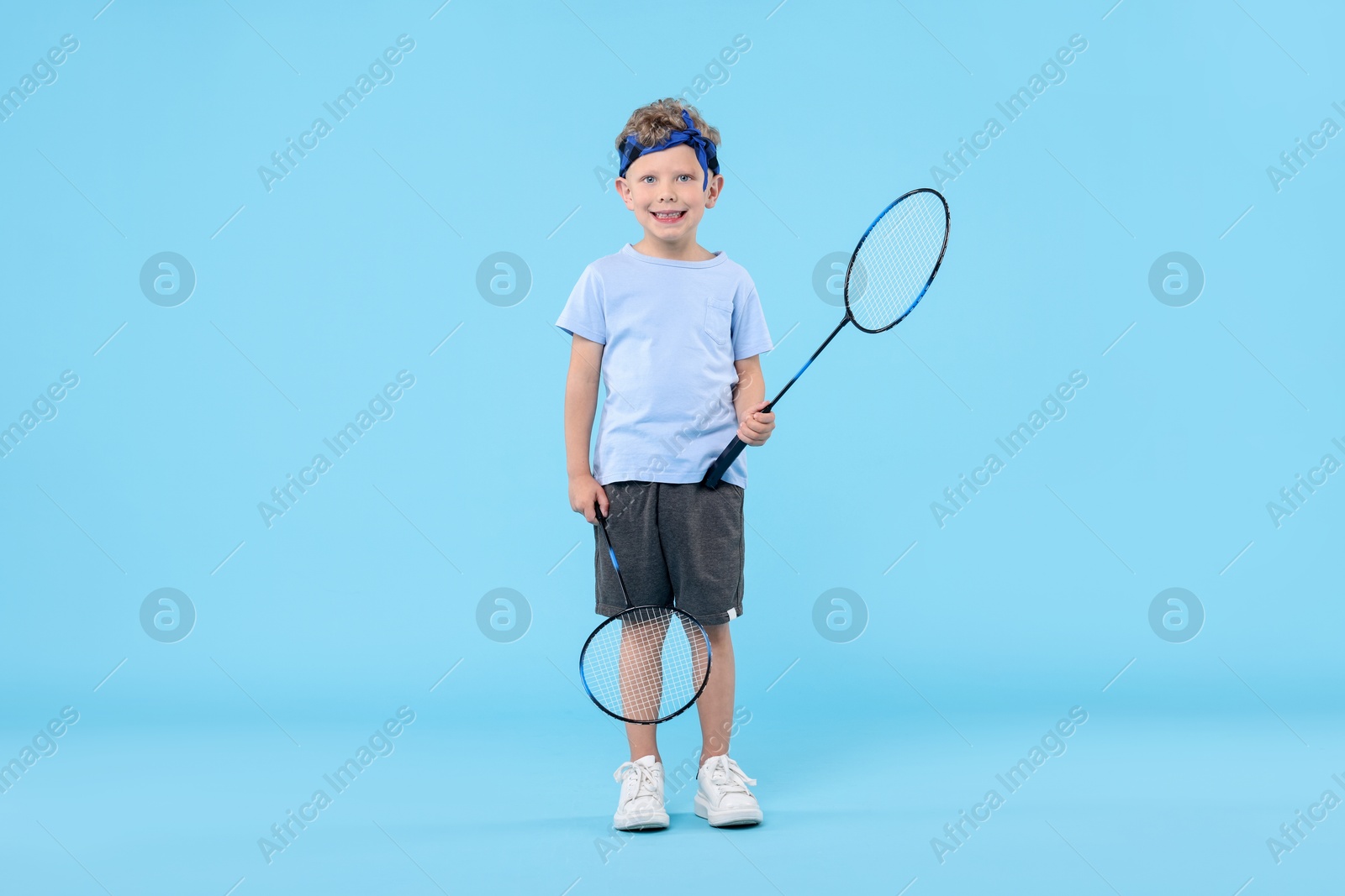 Little boy with badminton rackets on light blue background Photo of Little boy with badminton rackets on light blue background